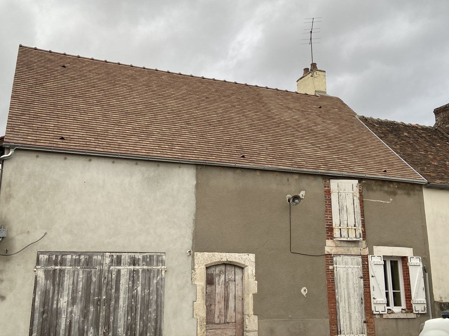 Toiture en tuiles plates rénovée avec gouttière neuve sur une maison ancienne