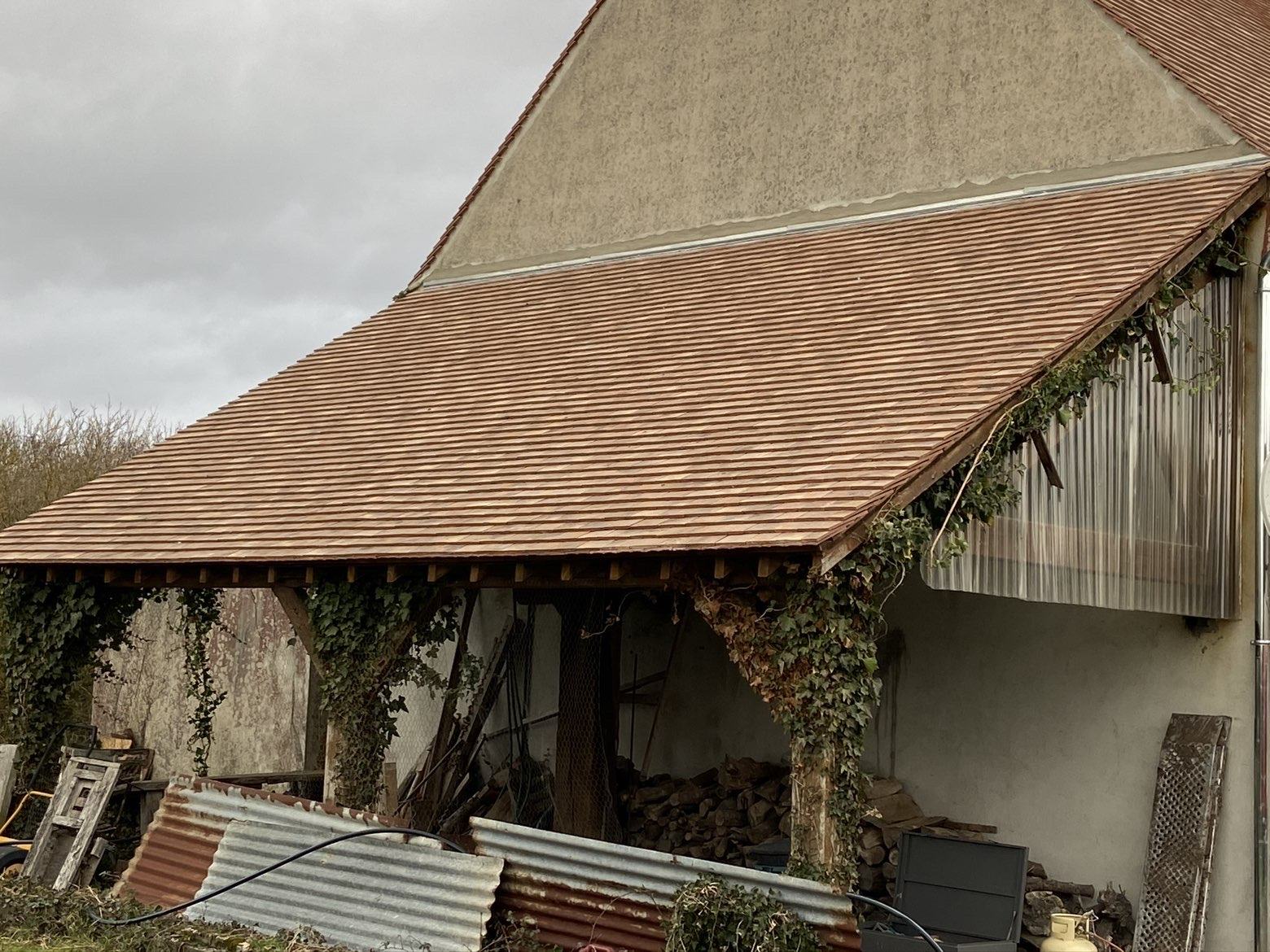 Auvent en tuiles neuves posé sur charpente bois à côté d’un corps de ferme